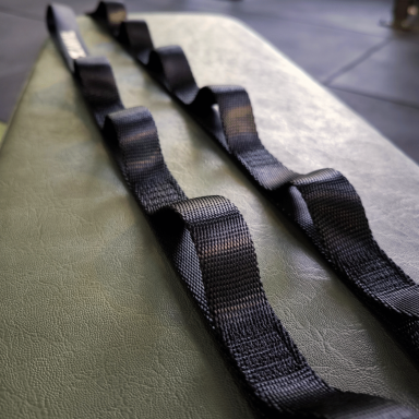 Schwarzer Trainingsgurt mit mehreren Schlaufen auf einer grünen Unterlage.